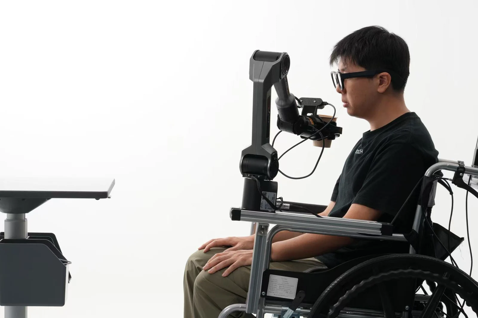 A seated participant using AR glasses with an assistive robotic arm in a prototype demonstration